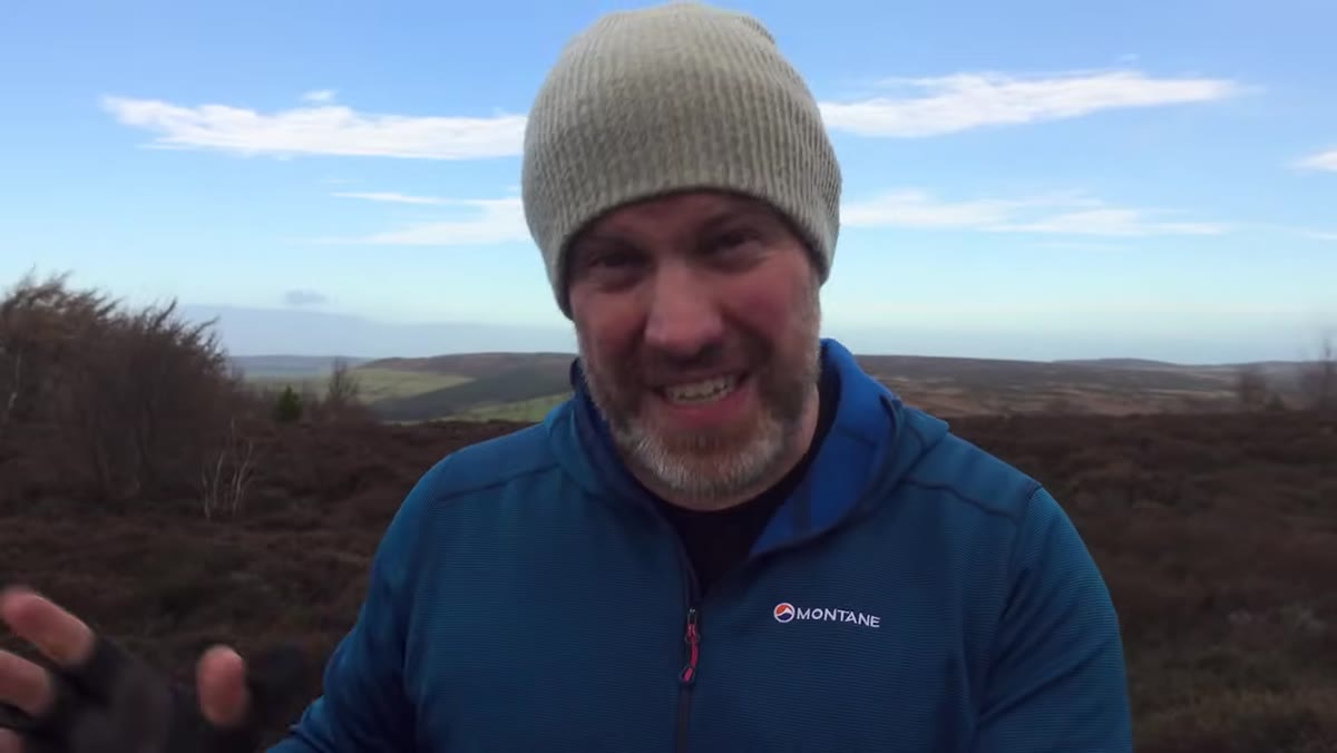 Adam gesturing toward his hiking boots on the trail