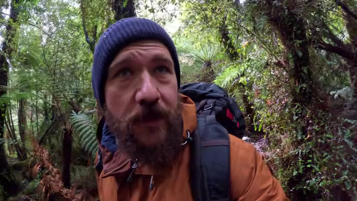 Photographer pushing through dense forest following a creek