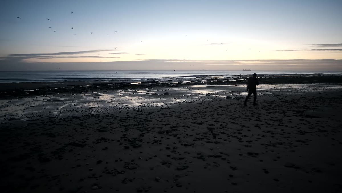 Thomas Heaton standing on a rocky, sand-stripped beach at dawn